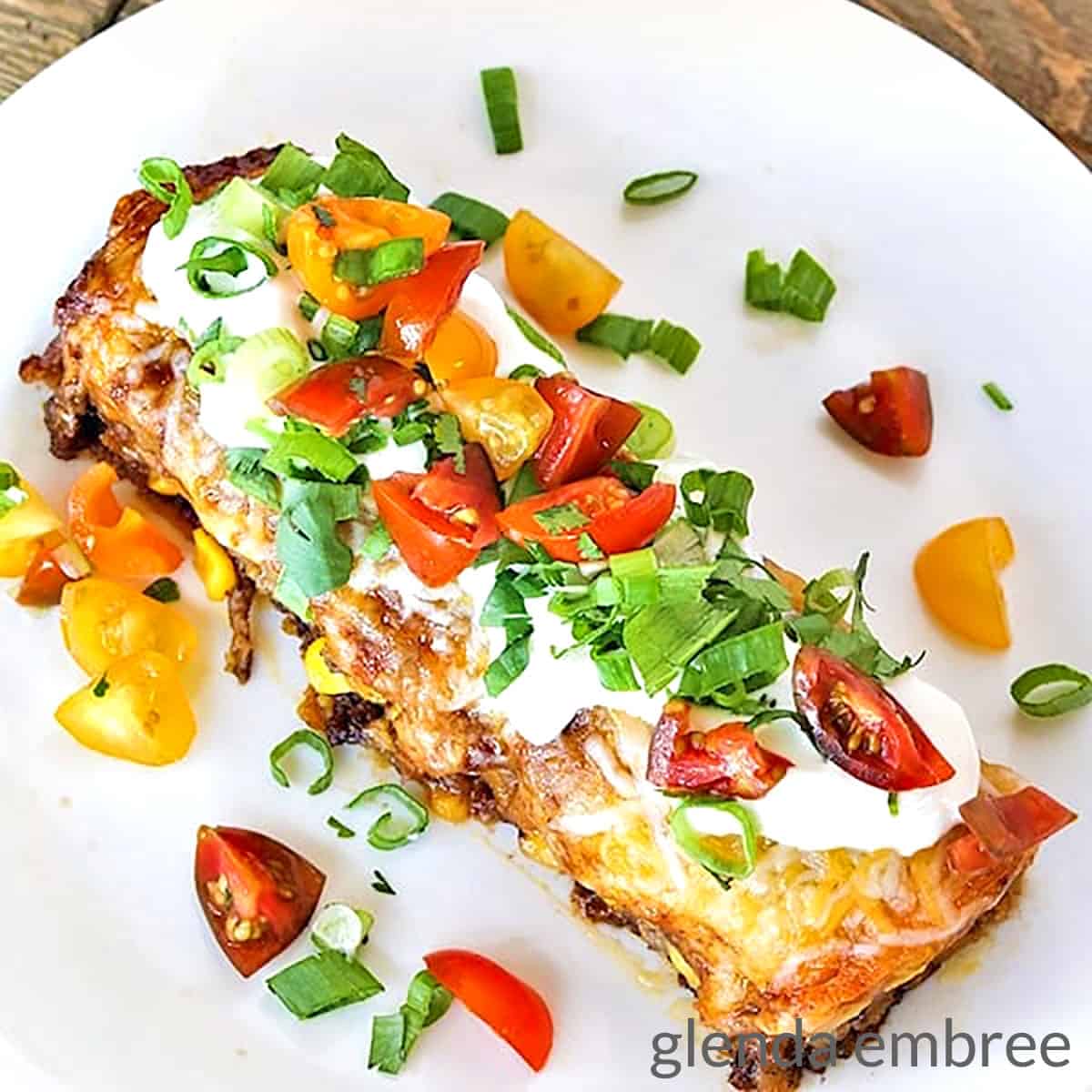 Beef Enchilada Casserole on a White plate sitting on a wooden table.