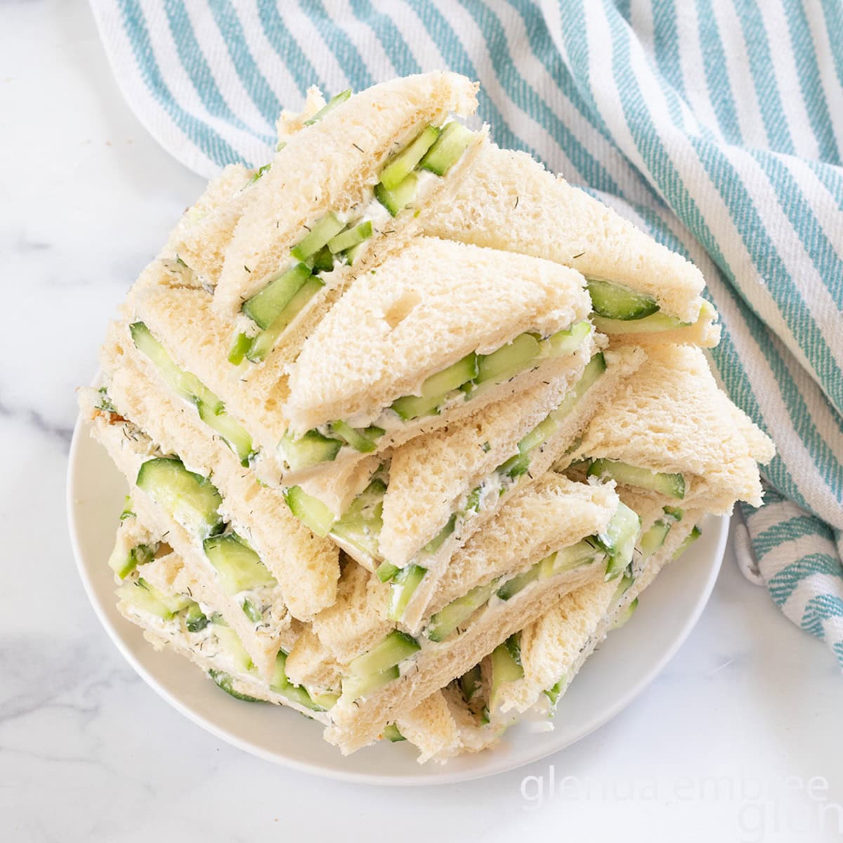 Cucumber Sandwiches stacked on a white plate.
